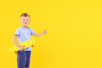 Photo of Little boy with penny board showing thumbs up on yellow background, space for text