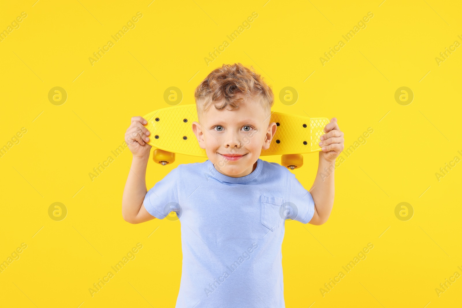 Little boy with penny board on yellow background Photo of Little boy with penny board on yellow background