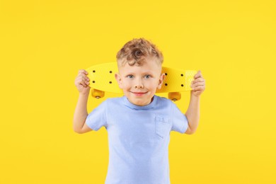 Photo of Little boy with penny board on yellow background