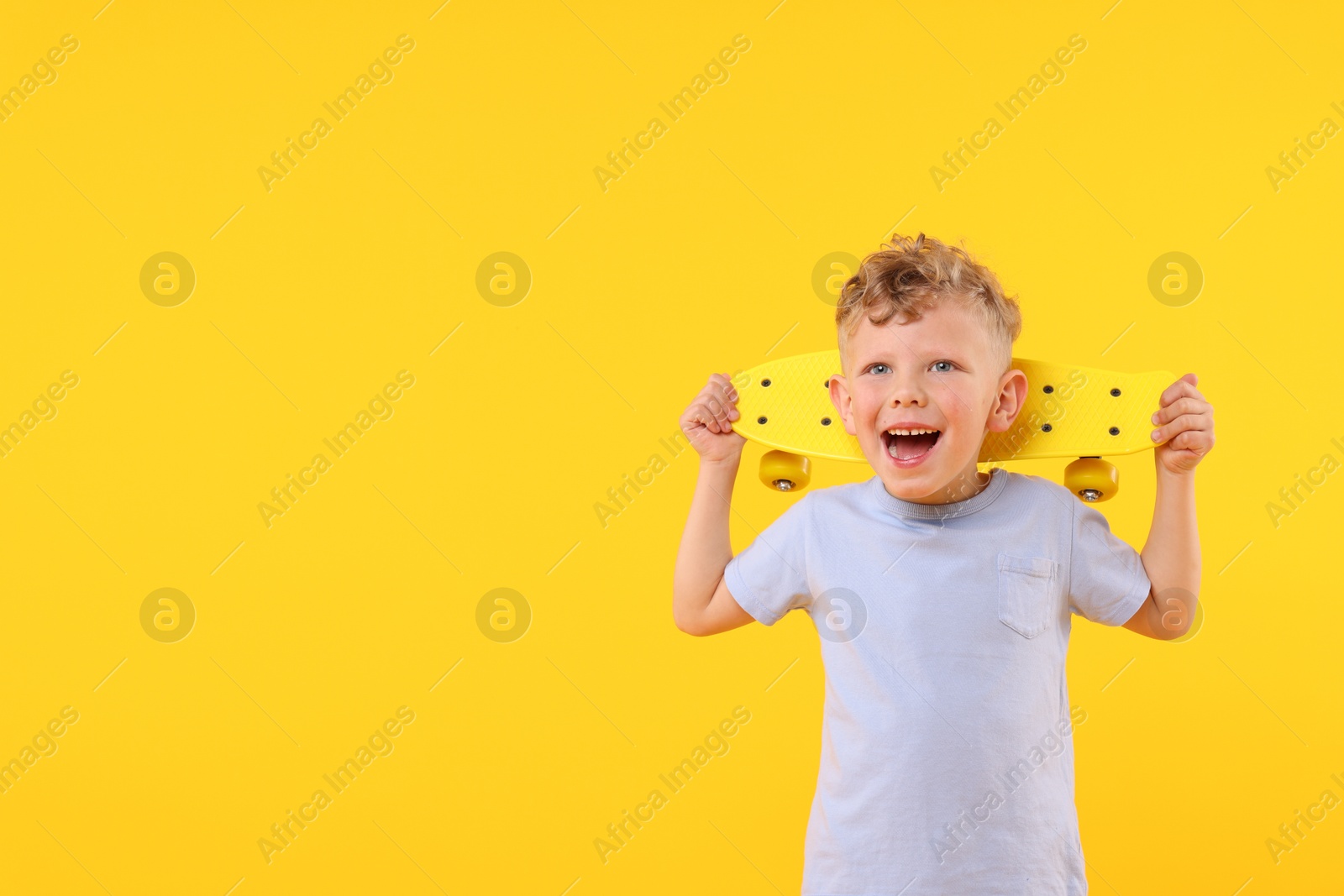 Cheerful little boy with penny board on yellow background, space for text Photo of Cheerful little boy with penny board on yellow background, space for text