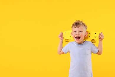 Photo of Cheerful little boy with penny board on yellow background, space for text