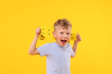 Photo of Cheerful little boy with penny board on yellow background