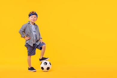 Photo of Little boy with soccer ball on yellow background, space for text