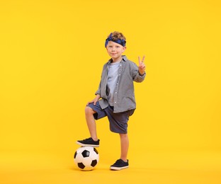 Photo of Little boy with soccer ball showing V-sign on yellow background