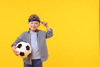 Photo of Little boy with soccer ball on yellow background, space for text