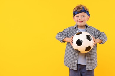 Photo of Little boy with soccer ball on yellow background, space for text