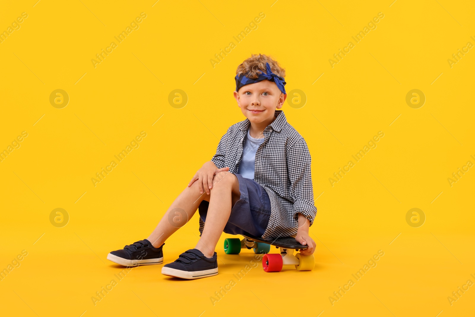 Little boy sitting on penny board against yellow background Photo of Little boy sitting on penny board against yellow background