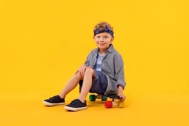 Photo of Little boy sitting on penny board against yellow background
