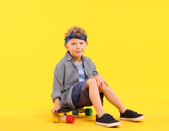 Photo of Little boy sitting on penny board against yellow background