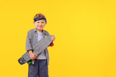 Photo of Little boy with penny board on yellow background, space for text
