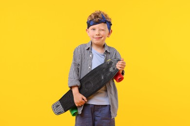 Photo of Little boy with penny board on yellow background