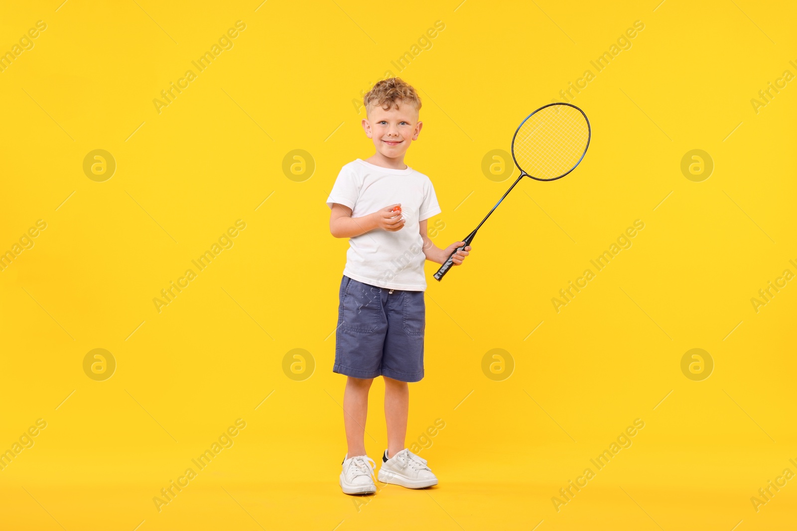 Little boy with badminton racket and shuttlecock on yellow background Photo of Little boy with badminton racket and shuttlecock on yellow background
