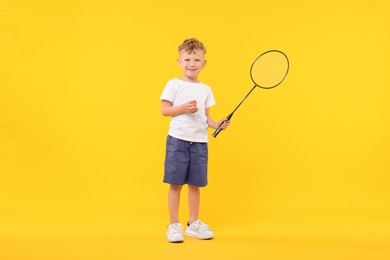 Photo of Little boy with badminton racket and shuttlecock on yellow background