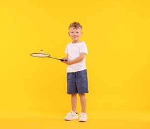 Photo of Little boy with badminton racket and shuttlecock on yellow background
