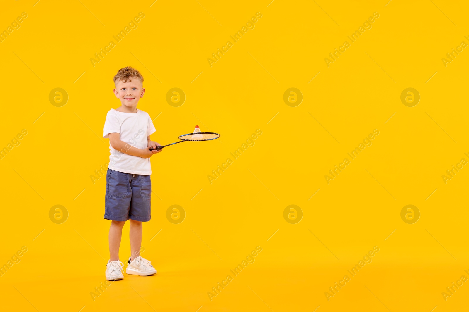 Little boy with badminton racket and shuttlecock on yellow background, space for text Photo of Little boy with badminton racket and shuttlecock on yellow background, space for text