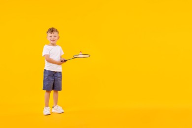 Photo of Little boy with badminton racket and shuttlecock on yellow background, space for text