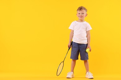 Photo of Little boy with racket and tennis ball on yellow background, space for text