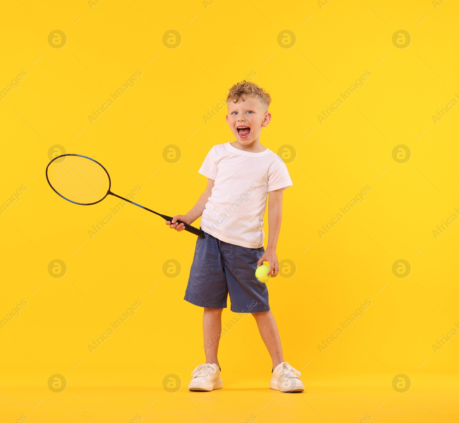 Cheerful little boy with racket and tennis ball on yellow background Photo of Cheerful little boy with racket and tennis ball on yellow background