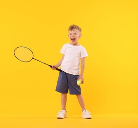 Photo of Cheerful little boy with racket and tennis ball on yellow background