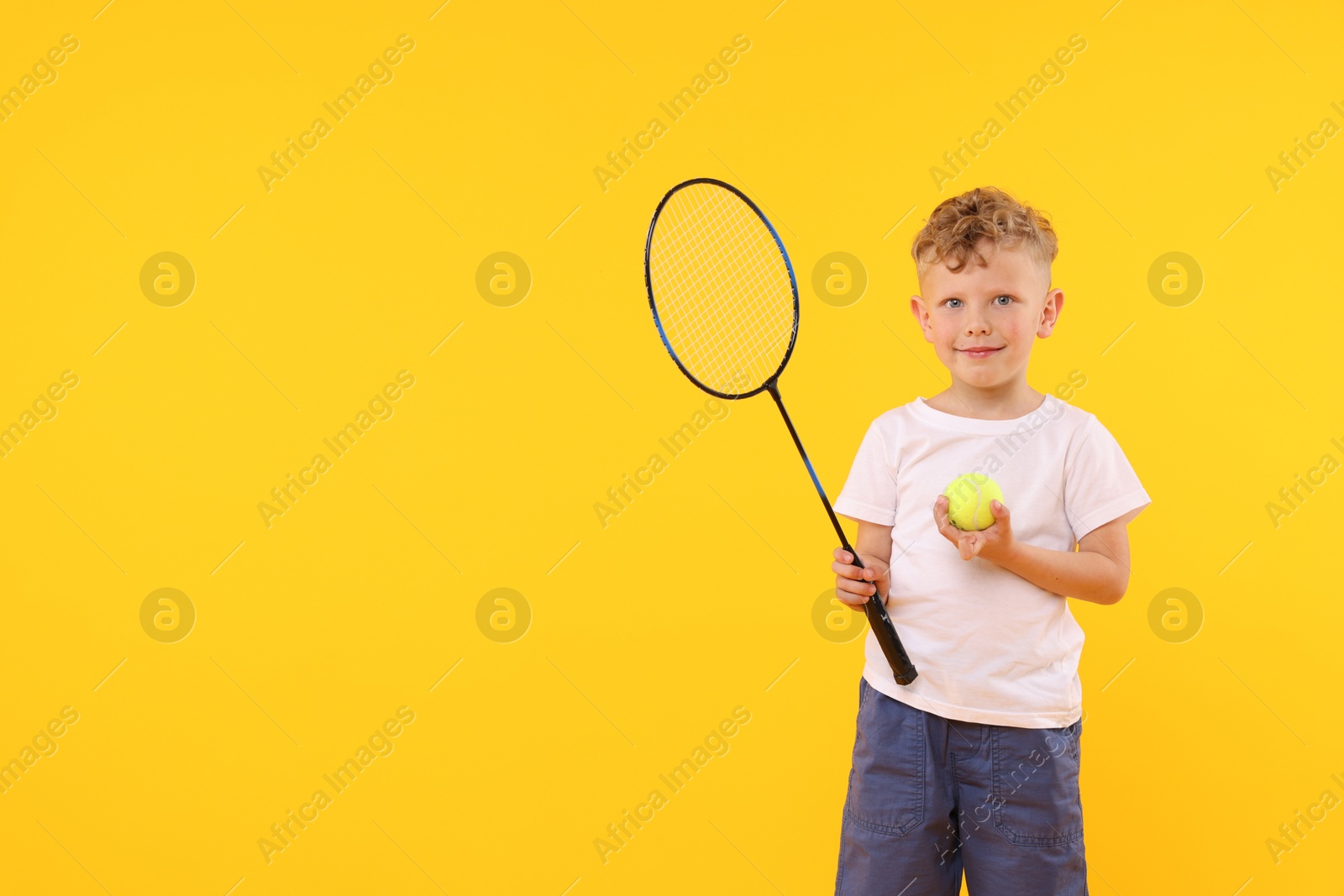 Little boy with racket and tennis ball on yellow background, space for text Photo of Little boy with racket and tennis ball on yellow background, space for text