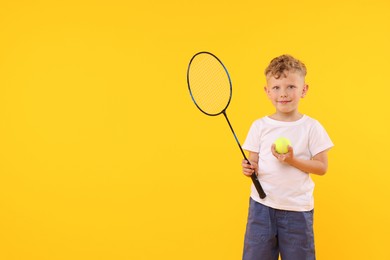 Photo of Little boy with racket and tennis ball on yellow background, space for text