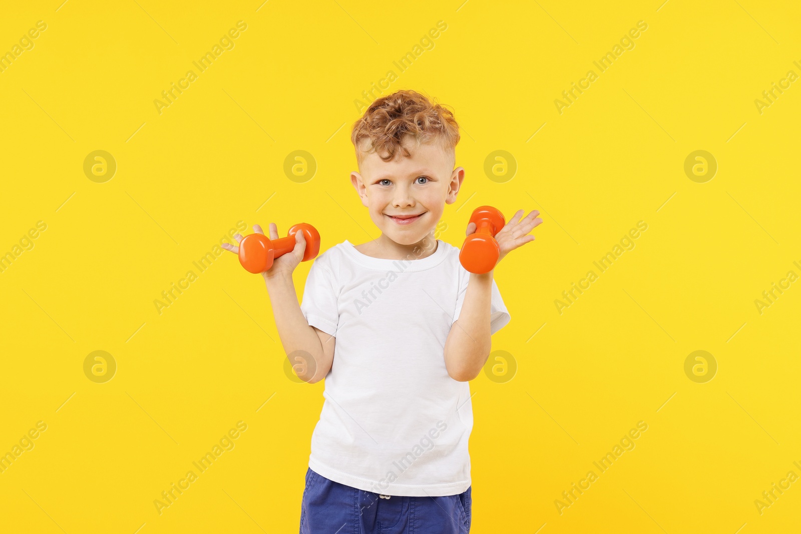 Little boy exercising with dumbbells on yellow background Photo of Little boy exercising with dumbbells on yellow background