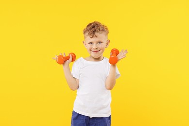 Photo of Little boy exercising with dumbbells on yellow background