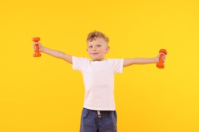 Photo of Little boy exercising with dumbbells on yellow background