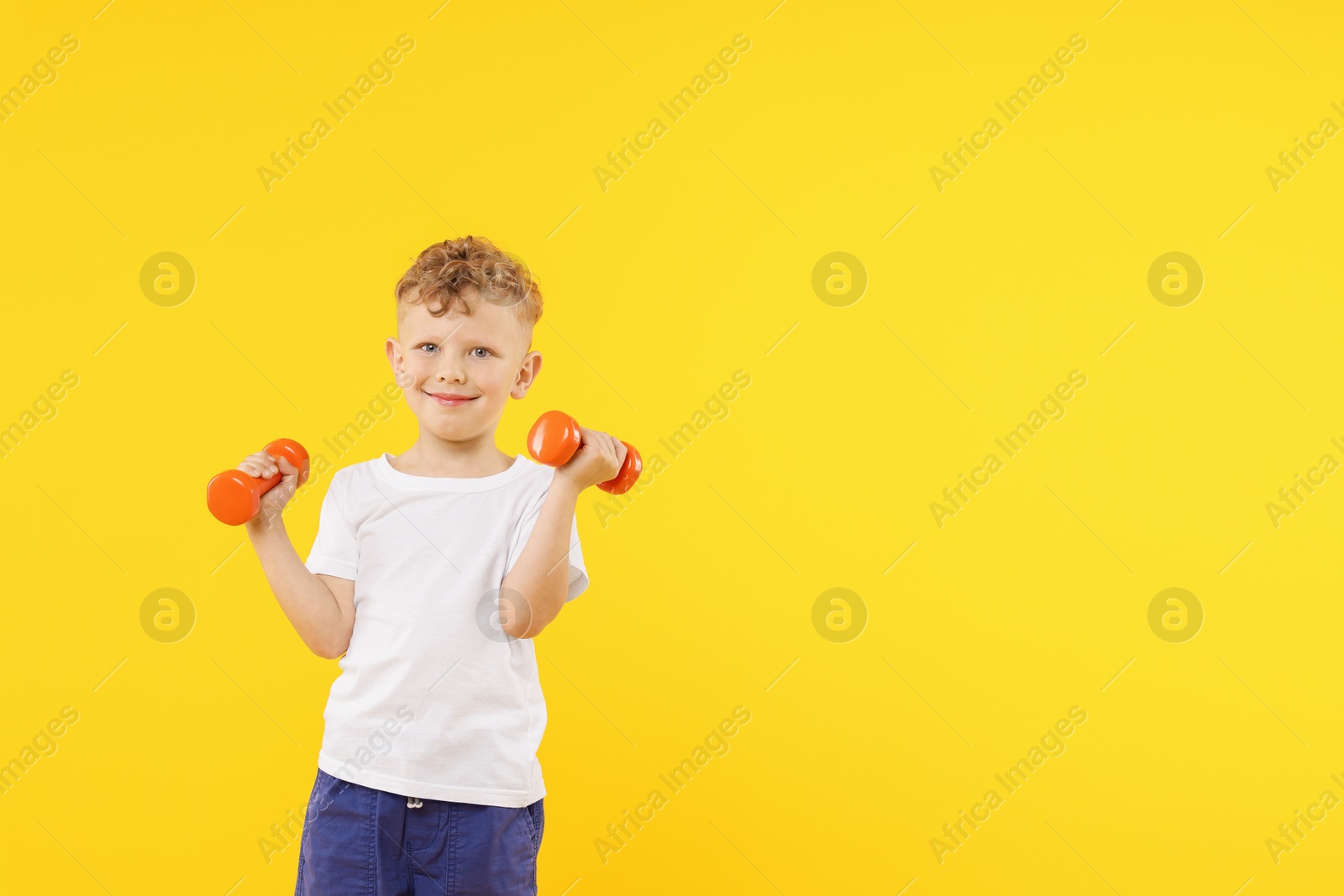 Little boy exercising with dumbbells on yellow background, space for text Photo of Little boy exercising with dumbbells on yellow background, space for text