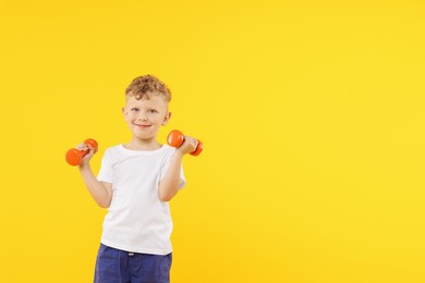 Photo of Little boy exercising with dumbbells on yellow background, space for text