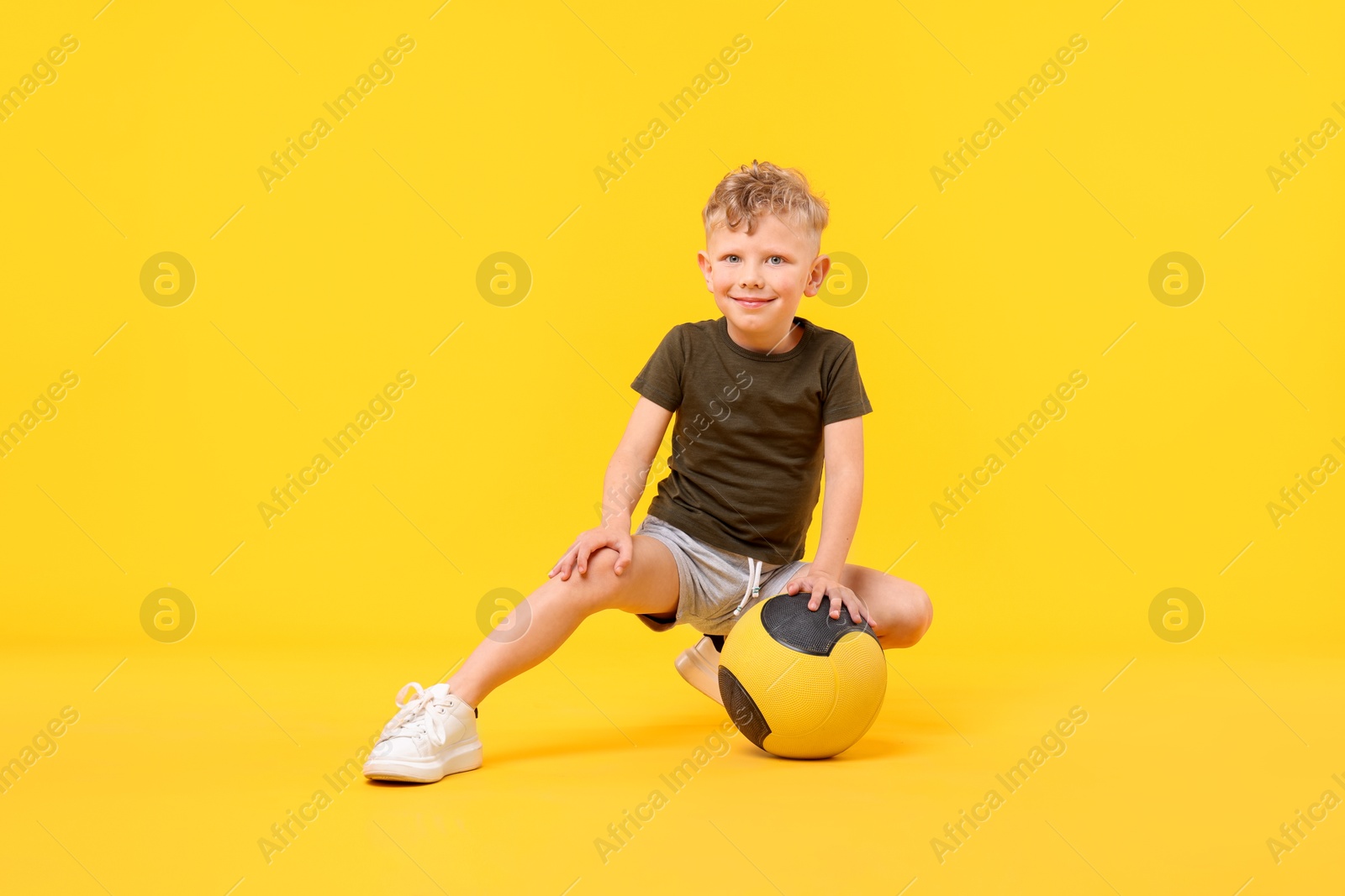 Little boy with medicine ball on yellow background Photo of Little boy with medicine ball on yellow background