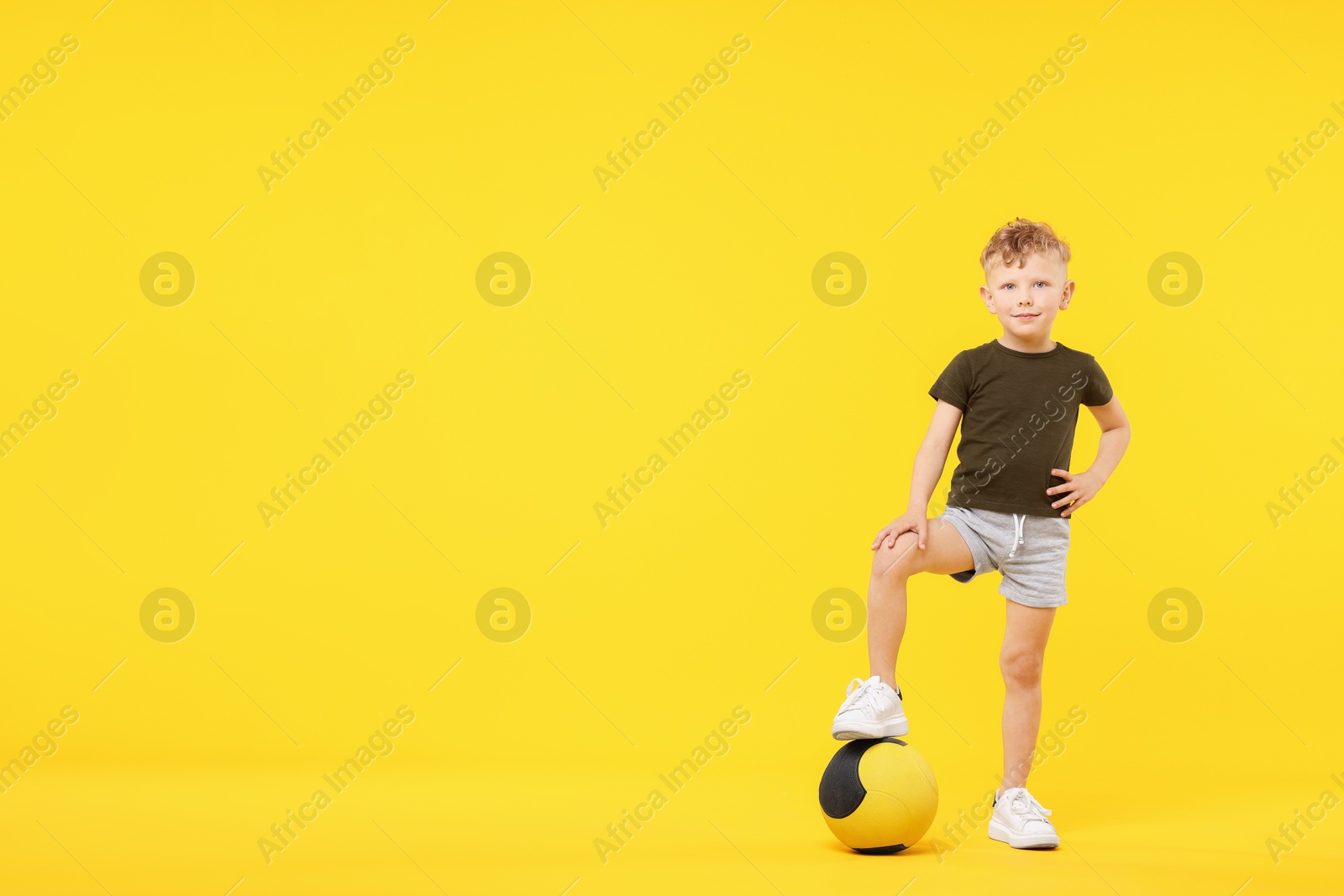 Little boy with medicine ball on yellow background, space for text Photo of Little boy with medicine ball on yellow background, space for text