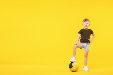 Photo of Little boy with medicine ball on yellow background, space for text