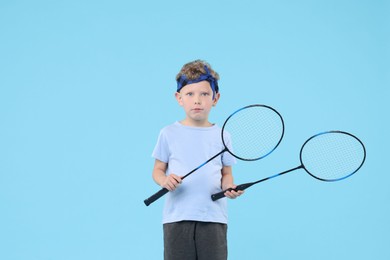 Photo of Little boy with badminton rackets on light blue background