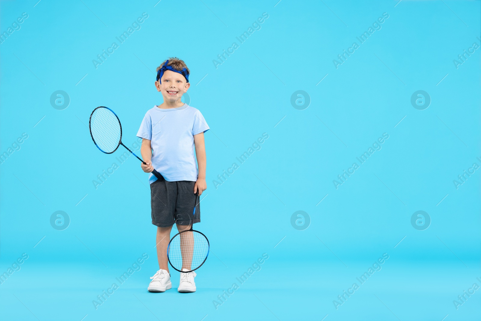 Little boy with badminton rackets on light blue background, space for text Photo of Little boy with badminton rackets on light blue background, space for text