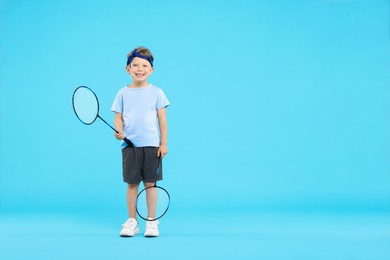 Photo of Little boy with badminton rackets on light blue background, space for text