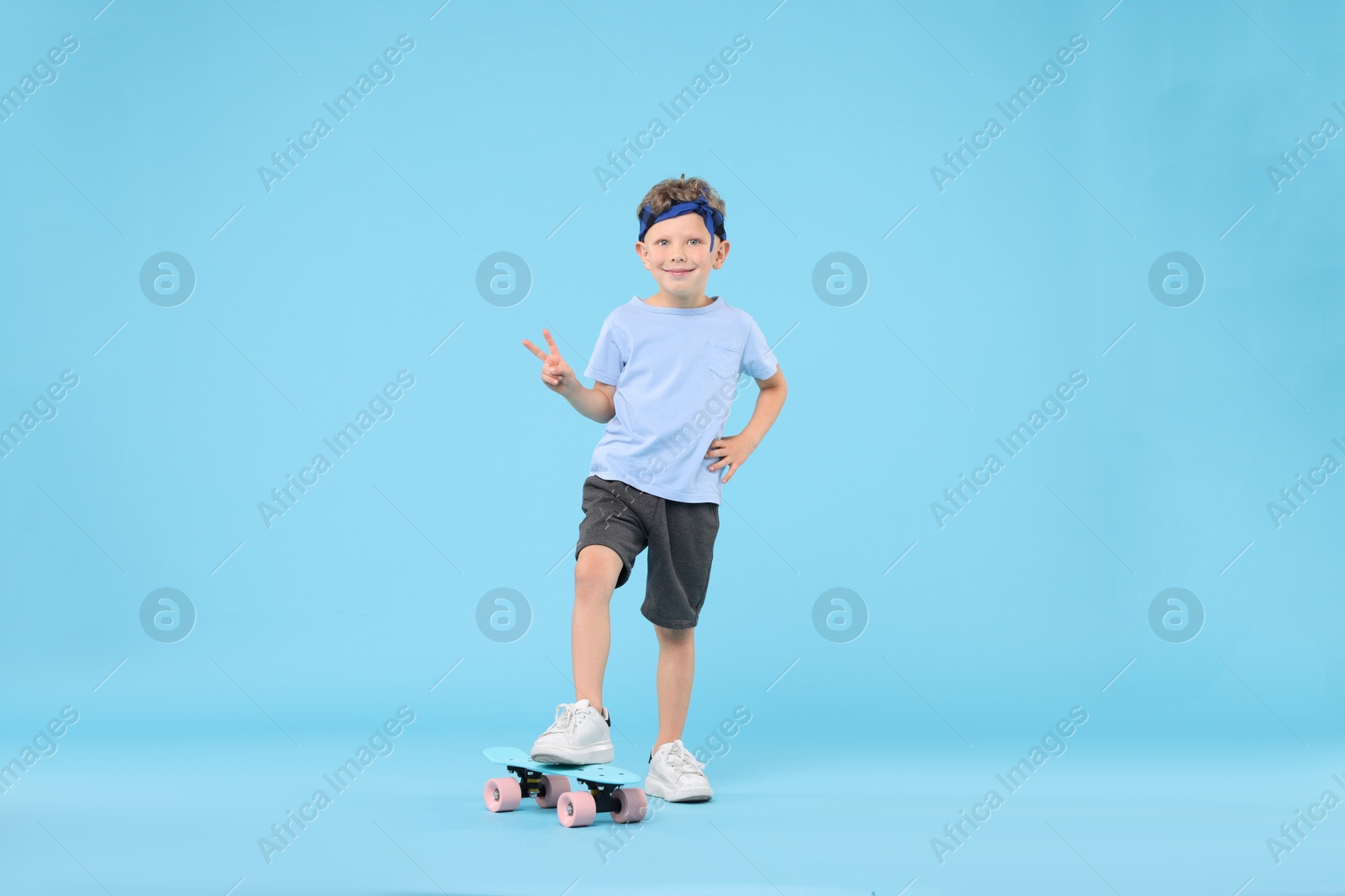 Little boy with penny board showing V-sign on light blue background Photo of Little boy with penny board showing V-sign on light blue background