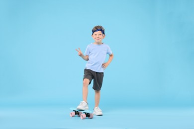 Photo of Little boy with penny board showing V-sign on light blue background
