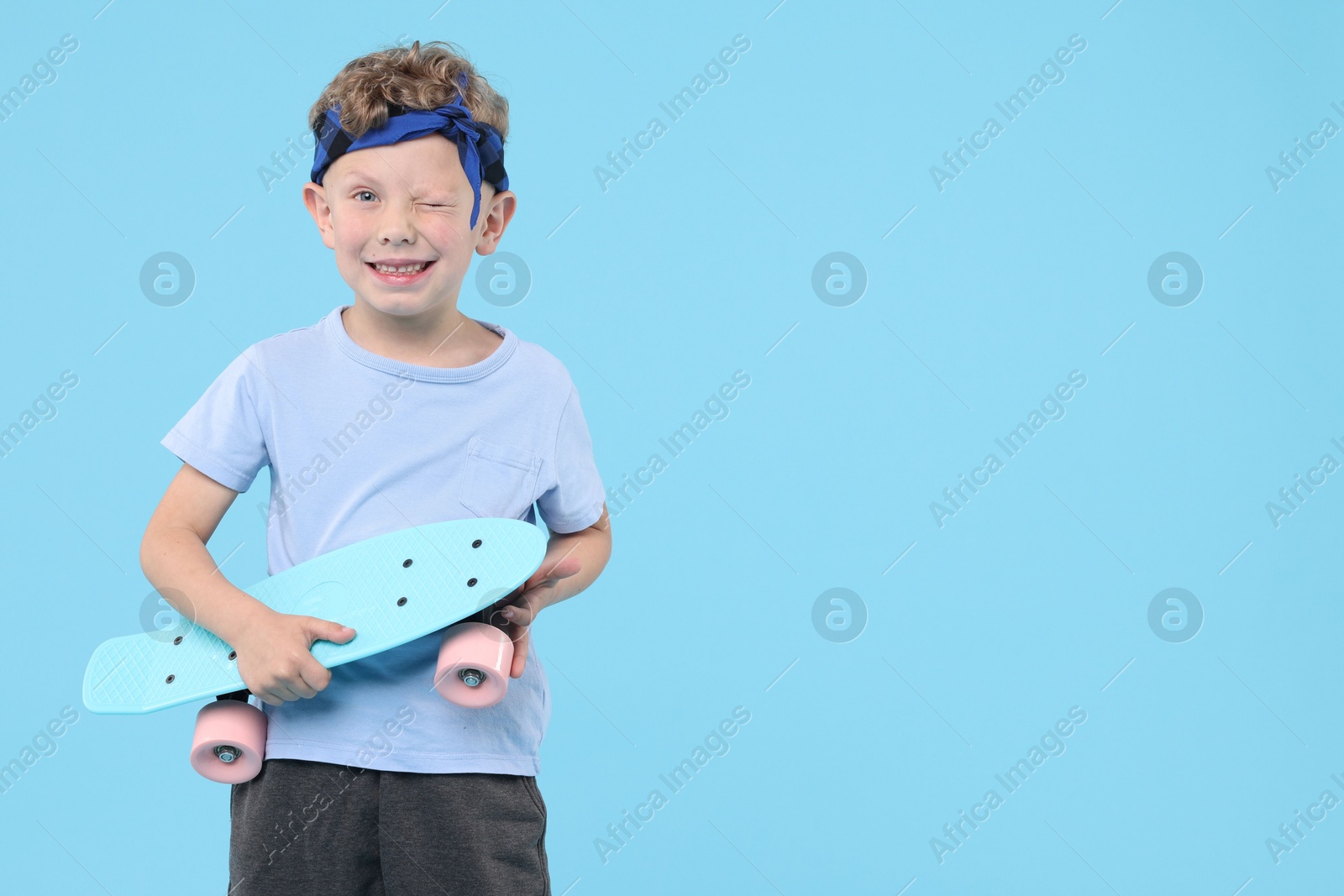 Little boy with penny board on light blue background, space for text Photo of Little boy with penny board on light blue background, space for text