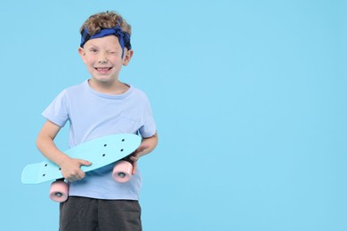 Photo of Little boy with penny board on light blue background, space for text