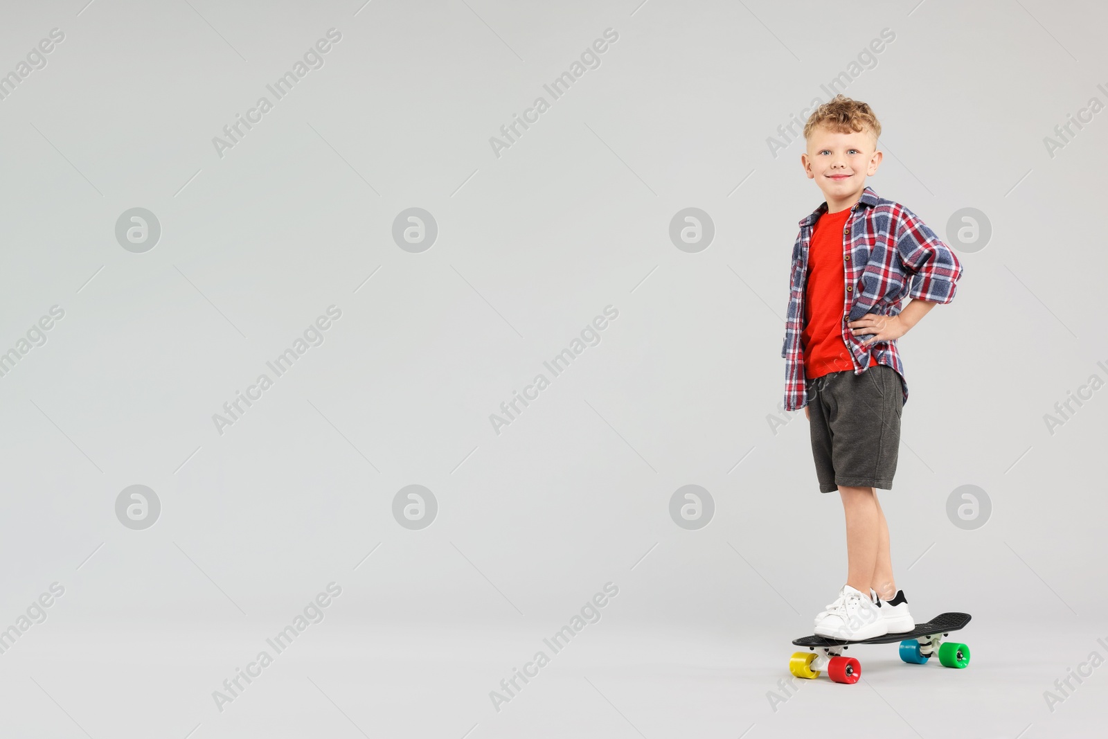Little boy standing on penny board against gray background, space for text Photo of Little boy standing on penny board against gray background, space for text