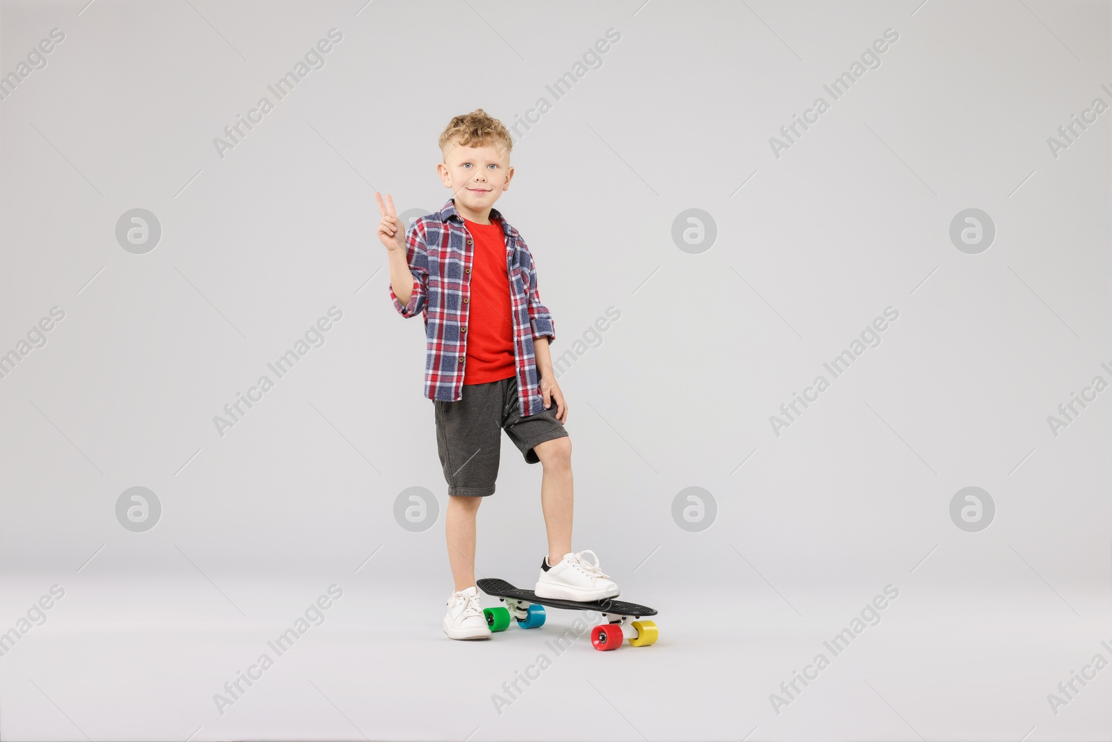 Little boy with penny board showing V-sign on gray background Photo of Little boy with penny board showing V-sign on gray background