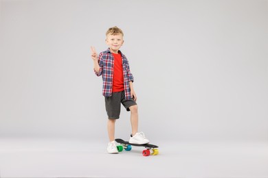 Photo of Little boy with penny board showing V-sign on gray background