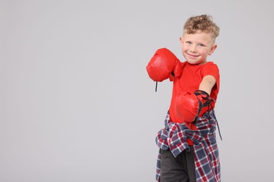 Photo of Little boy with boxing gloves on gray background, space for text