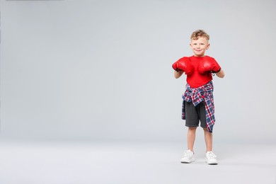 Photo of Little boy with boxing gloves on gray background, space for text