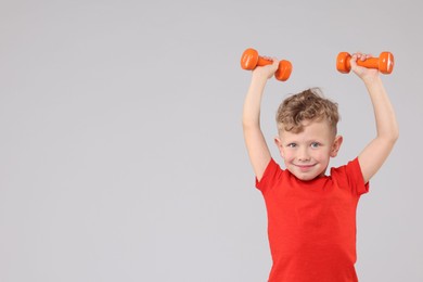 Photo of Little boy exercising with dumbbells on gray background, space for text