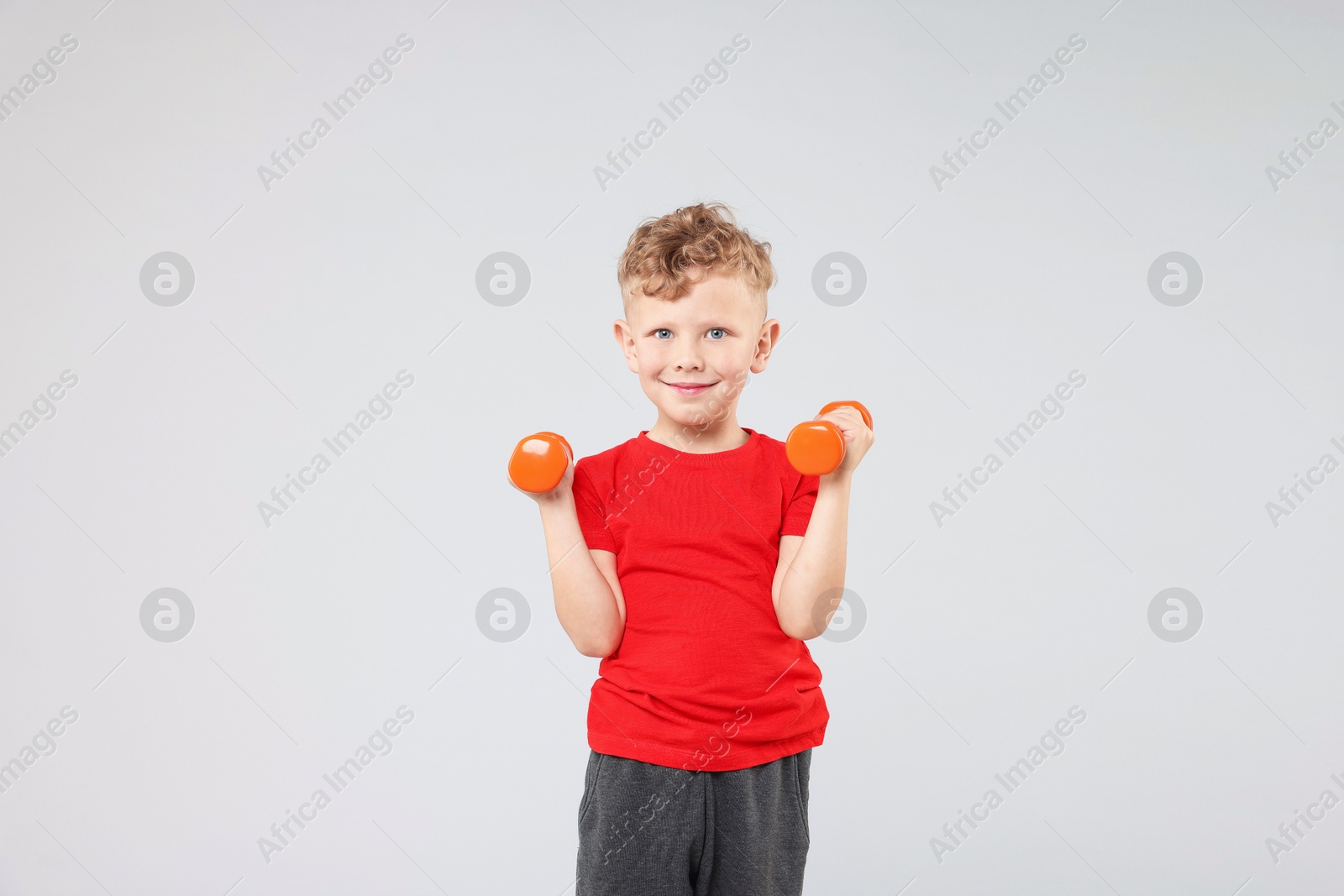Photo of Little boy exercising with dumbbells on gray background