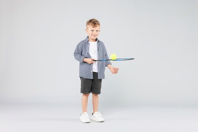 Photo of Little boy with racket and tennis ball on gray background