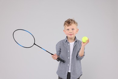 Photo of Little boy with racket and tennis ball on gray background