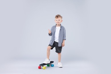 Photo of Little boy with penny board showing thumbs up on gray background